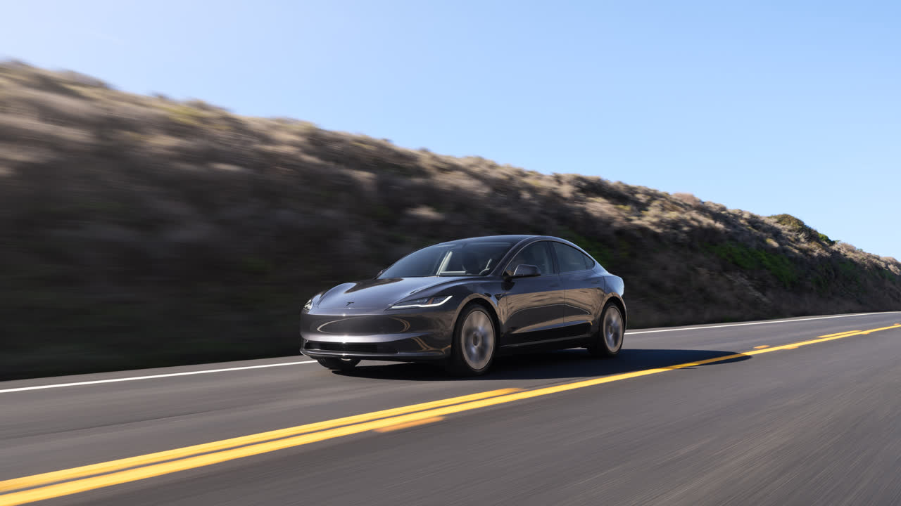 Mørkegrå Tesla Model 3 i fart på en landevej langs en bakkeskråning. Model 3 blev nummer to blandt de mest solgte biler i Danmark i september 2026, kun overgået af Tesla Model Y